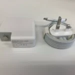 A 61W USB-C power adapter and coiled USB-C charging cable with a UK three-pin plug, included with the Apple MacBook Air 2020 M1 256GB/16GB, are placed on a white surface.