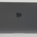 A closed, space gray Apple MacBook Air 2020 M1 (256GB/16GB) rests on a white surface, with the black Apple logo centered on its lid.