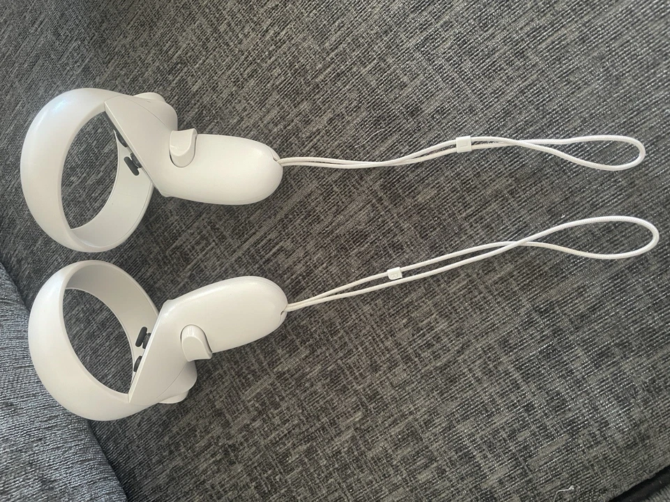 The Meta Quest 2 Virtual Reality Headset 128GB controllers, in white with wrist straps, are shown resting on a textured gray fabric surface.