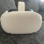 A Meta Quest 2 Virtual Reality Headset 128GB with Controllers sits on a gray upholstered couch, with a patterned pillow in the background.