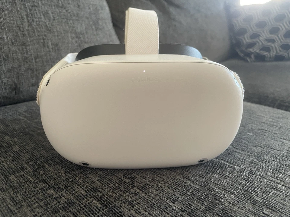 A Meta Quest 2 Virtual Reality Headset 128GB with Controllers sits on a gray upholstered couch, with a patterned pillow in the background.